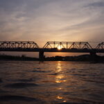 西の空にだんだん沈む夕日を背景にした渡良瀬橋の写真です。