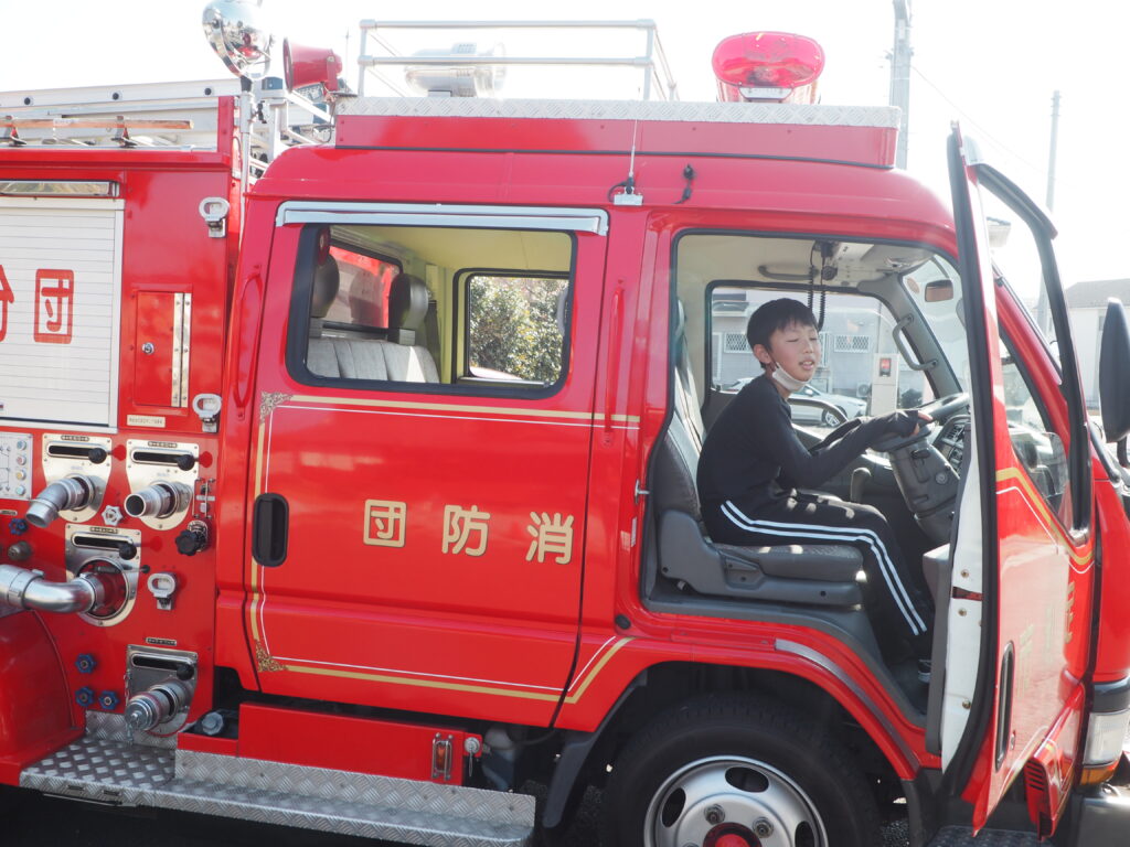 消防車に乗る地域の少年の写真です。