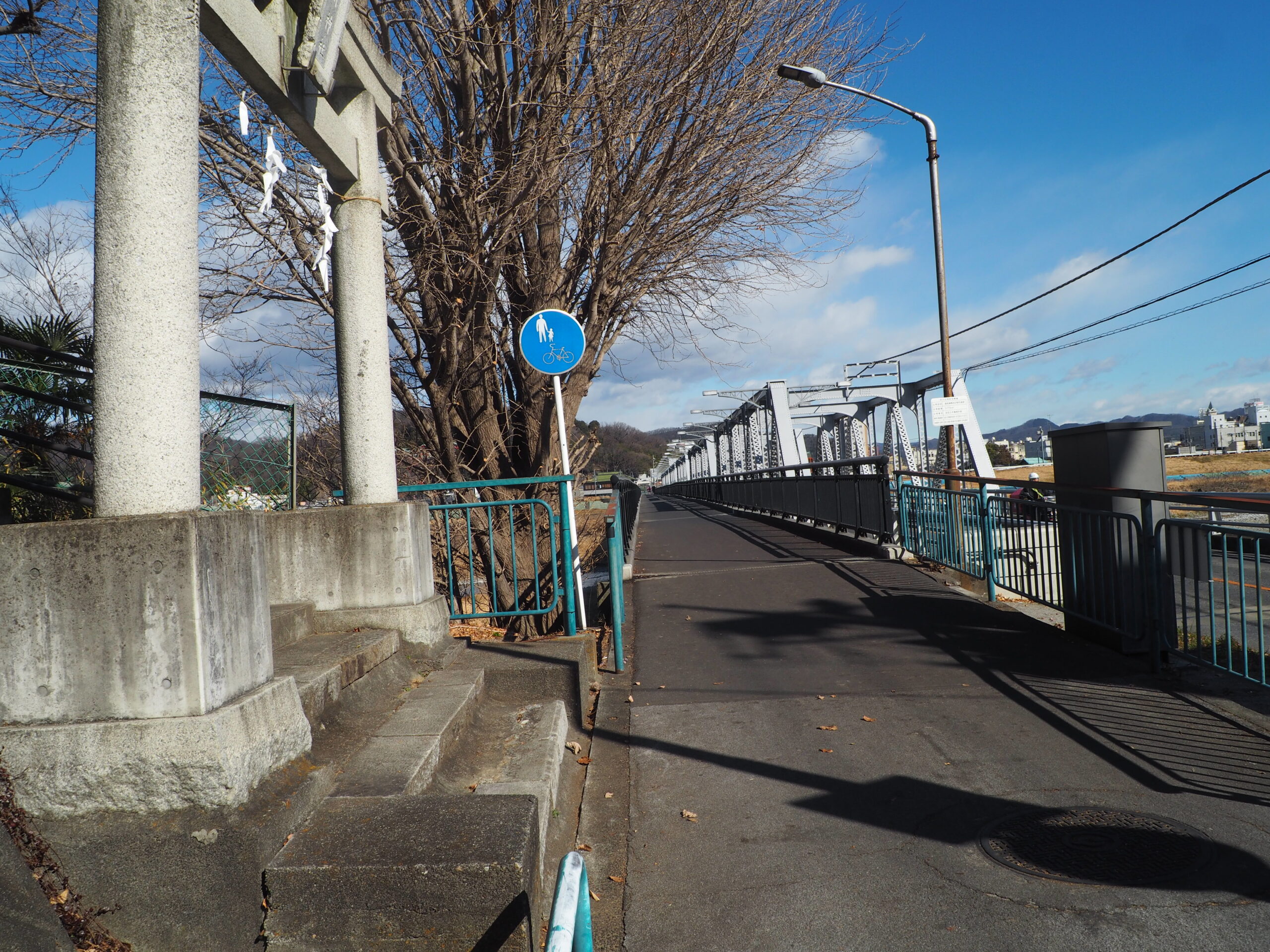 左手側に鳥居、前方に渡良瀬橋が見える風景写真です。