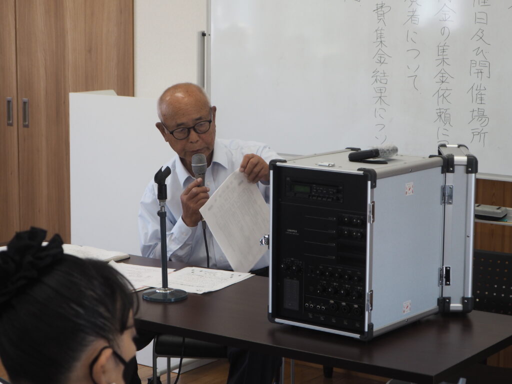第２回役員・隣組超会議で赤い羽根募金を活用した放送設備を紹介する自治会長の写真です。